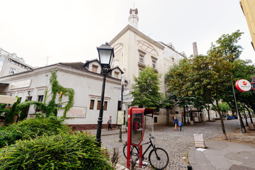 Fototapeta premium Belgrade, Serbia - June 16, 2018. Historic place Skadarlija with phone booth, trees, lamppost, bicycle and cobbled lane in downtown. Bohemian street with bars, restaurants and murals.