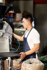 Young male factory worker in apron standing near the machine and controlling the process of production on the plant