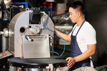Young Asian operator standing looking at machinery equipment and controlling the process of...