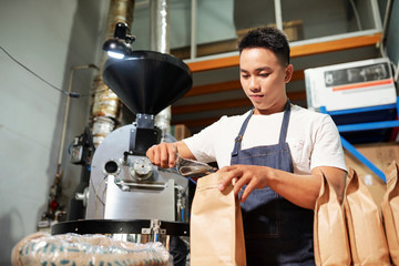 Seller in uniform filling bags with coffee beans working in the coffee factory