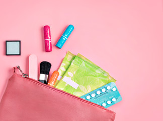 Lady's bag. Sanitary pads and tampons in cosmetic bag on pink background. Concept of critical days, menstruation