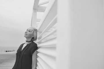 monochrome portrait of pretty cool beautiful short hair blonde woman in short summer dress near wooden white arbor for the beach by the sea