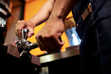 Close-up of waiter preparing espresso in coffee shop he grinding coffee beans with grinder