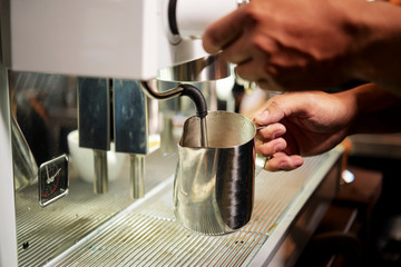 Close-up of man holding coffeepot and brewing a fresh hot coffee into it with coffee machine in cofee shop