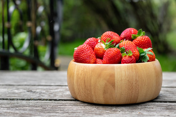 Sweet fresh juicy organic ripe strawberries in wooden bowl on wooden surface outdoors in garden or...
