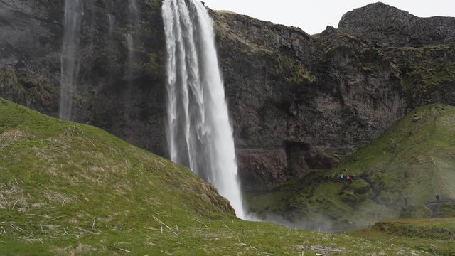 Side view of the majestic waterfall Seljalandsfoss located in Iceland. Massive amount of tourists all taking the same pictures in the background.
