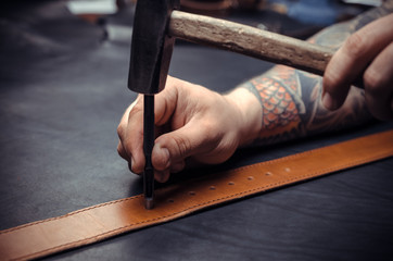 Professional Leather Worker cuts out leather goods at his tanning shop - obrazy, fototapety, plakaty
