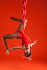 A young blonde girl with long hair in a red suit performs gymnastic and exercises on silk. Studio...