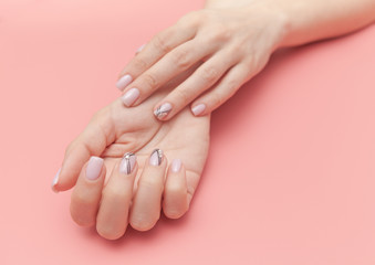 Tender hands with perfect nude manicure on trendy pastel pink background. concept of healthy and beautiful hands.