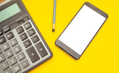 Modern calculator and phone with space for text on a yellow background, top view