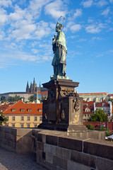 Fototapeta na wymiar Statue of St John of Nepomuk on the Charles Bridge with St. Vitus Cathedral in background.