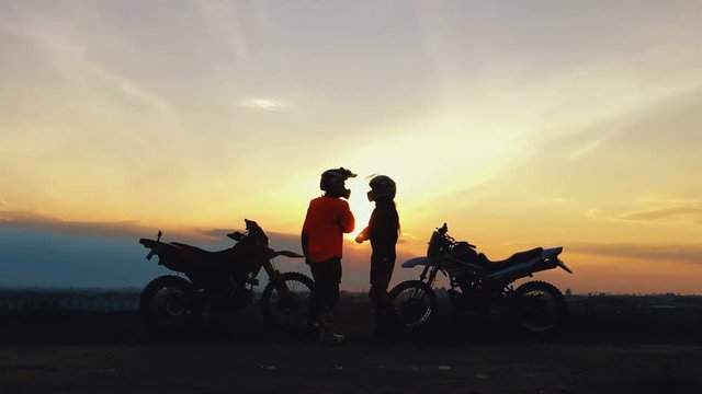 Two riders with their bikes greet each other with victory. Silhouettes of motorcycles and riders on the background of beautiful sunset. Enjoy the freedom. Enduro.