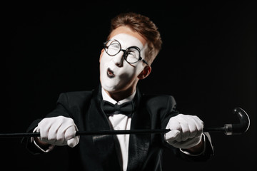 portrait of mime man in tuxedo and glasses with walking stick winks on black background