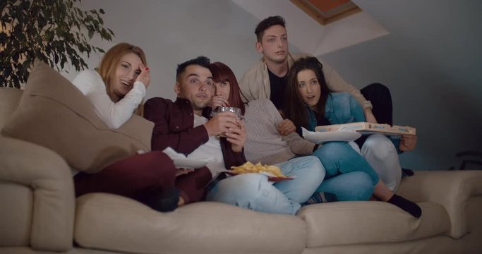 Friends eating pizza and chips on the sofa at home while watching TV. Shot in slow motion