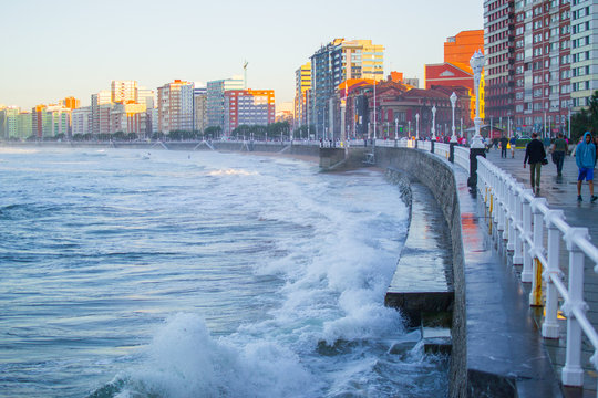 Waves splashing against the wall in San Lorenzo beach in Gijon, Asturias, Spain, with the promenade and buildings in one side