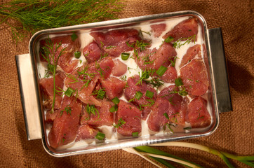 Marinated in milk and herbs, the meat in a steel pot on the cloth with fresh herbs