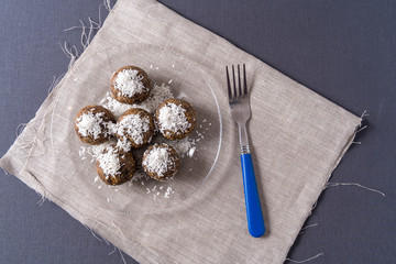 Healthy organic energy balls made with dates, prunes, raisins, peanut, with coconut shavings, in a glass plate on gray background.