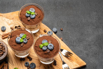 Classic tiramisu dessert in a glass with blueberries on dark concrete background