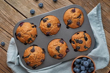 Blueberry muffin in tray, top view. Cupcakes with berries in baking dish on old linen napkin, rustic wooden table, breakfast with cake