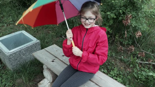  Cute little girl playing with umbrella and singing on bench in park
