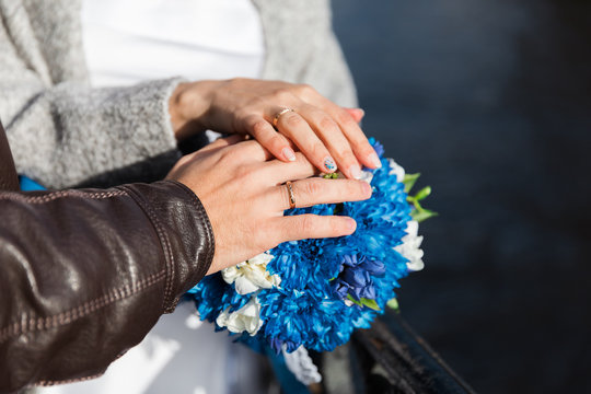 Hands with wedding rings on blue bridal bouquet