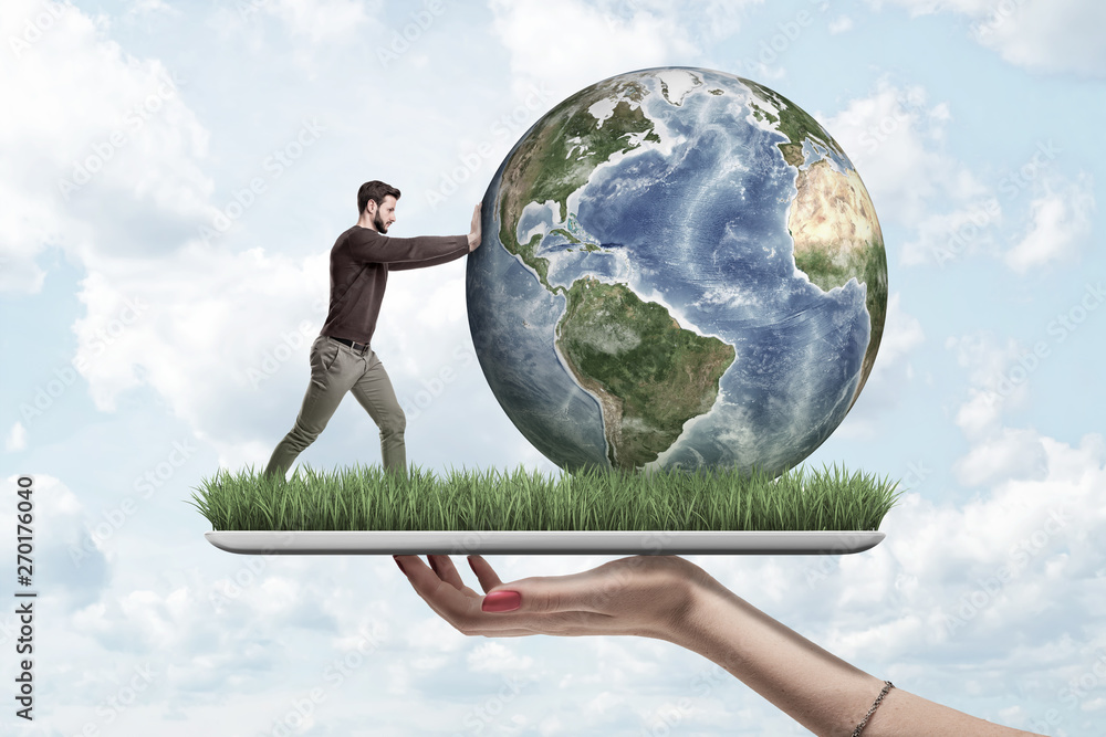 Wall mural Crop side view of woman's hand holding digital tablet with green grass growing on screen and little man pushing planet Earth on top.