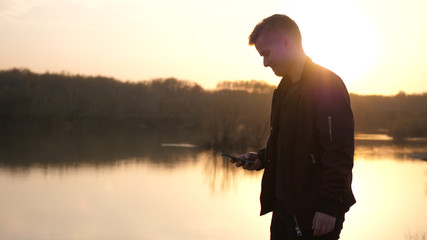 Young man uses smart phone at beautiful sunset on the beach.