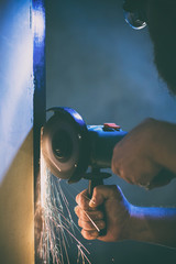 A man repairs a door in the basement of his house using a manual grinding machine.