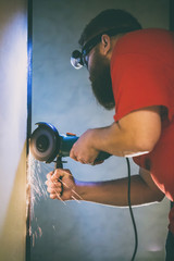 Naklejka premium A man repairs a door in the basement of his house using a manual grinding machine.