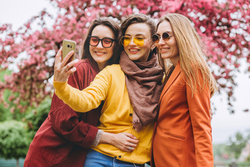 The best friends. Selfie - Three beautiful woman. Lifestyle. Beautiful young women in sunglasses dressed in the bright clothes smiling. girls make photo of against the background of flowering trees