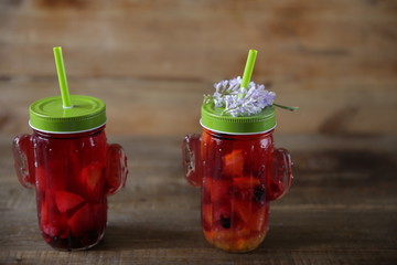 red compote of fresh berries and fruits in a glass jar with a straw for drinking  and flower on a table made of natural wood. Fresh summer drink. With copy space.