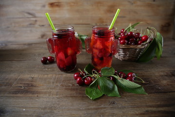 Berries and citrus infused water cocktail, compote, lemonade or tea. Summer iced cold drink with berries, cherry, lemon on a wooden rustic background with branch of cherry. With copy space for text.
