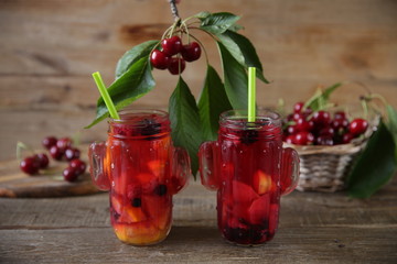 sweet compote of fresh berries and fruits in a glass jar with a straw for drinking with fresh berries of sweet cherry in a basket on a table made of natural wood. Fresh summer drink. With copy space.
