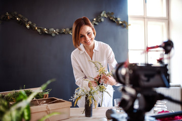 Young creative woman vlogger in a flower shop. A startup of florist business.