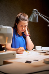 Young serious woman sitting at her workplace and concentrating on her work she drawing sketch with pencil at office