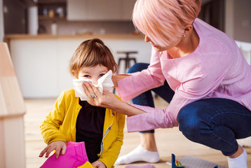 Mother blowing her small daughter's nose when playing at home.