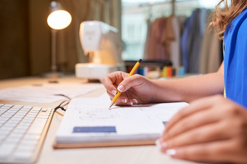 Close-up of female designer sitting at workplace and drawing with pencil in notebook or making notes about future plans
