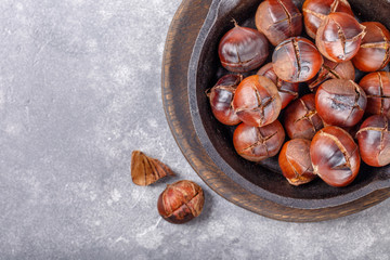 Obraz premium Roasted edible sweet chestnuts served in cast-iron skillet on gray background. Top view. Copy space.