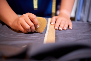 Close-up of fashion designer using ruler and drawing patterns with soap for cutting clothes in atelier