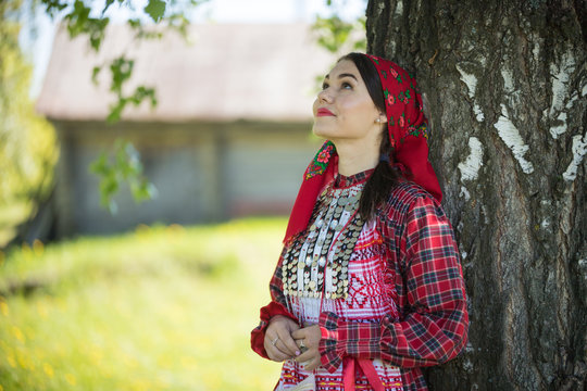 Young woman in traditional russian clothes standing under a tree and looking up