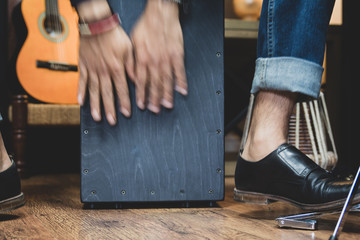 A stylish musician in denim and double monk shoes plays the Cajon, a Peruvian drum used commonly with Spain&rsquo;s Flamenco dance. 