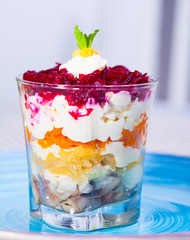 verrin glass with Russian salad herring under fur coat from vegetables on blue plate