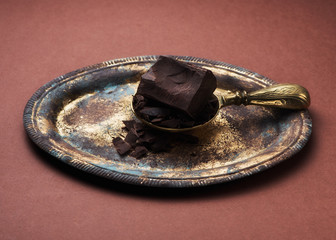 Chocolate on metal tray and brass scoop on brown background