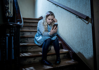 Sad depressed unhappy child suffering from cyberbullying by mobile smart phone sitting alone.