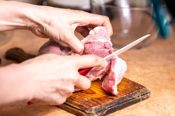 Female hands with a knife in their hand cut fresh meat on a wooden board