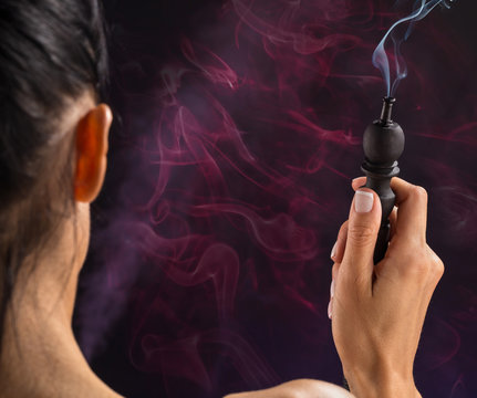 Hookah mouthpiece with a stream of smoke in a beautiful female hand on a dark background. Copy space.