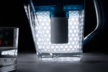 Glowing with many lights decanter for water purification is filled with purified water through a...