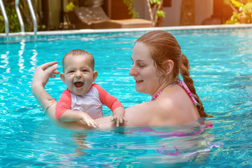 Happy little child with mother, Baby first time in a large pool and very impressed. Infant very happy and frolic.