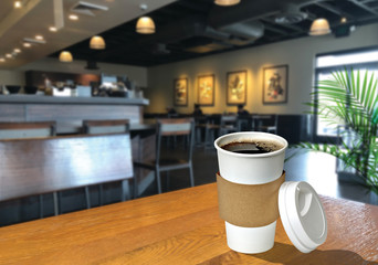 Black or dark coffee in takeaway cup on wooden table at cafe