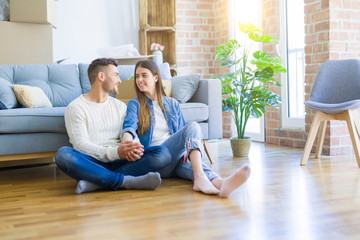 Young beautiful couple sitting on the floor of new apartment, smiling in love happy for moving to a new home